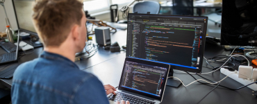 Ein Entwickler sitzt an seinem Laptop und programmiert an einer Anwendung.