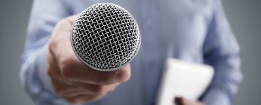 Hand, die ein Mikrofon hält, um ein Geschäftsinterview oder eine Pressekonferenz durchzuführen